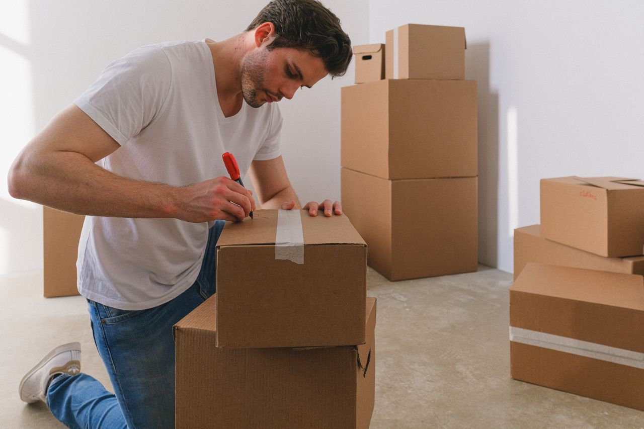 creative-02 A man labels cardboard boxes for moving, kneeling indoors with natural light.